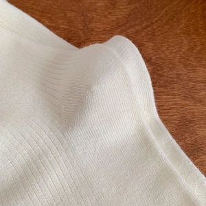 Macro detail of creamy white ribbed knit texture showing soft vertical patterns