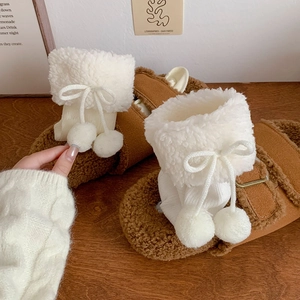 Detail of white knit socks with pom-poms and bows paired with fuzzy brown slippers
