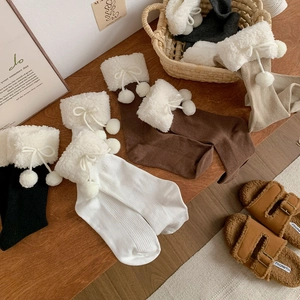 Detail of knitted mid-calf socks with plush pom-poms and fleece cuffs in warm autumn tones