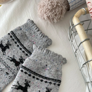 Close-up of grey wool socks featuring reindeer patterns and colorful nep yarn texture