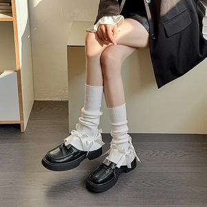Detail of white knit leg warmers with ribbon bows and black platform loafer shoes