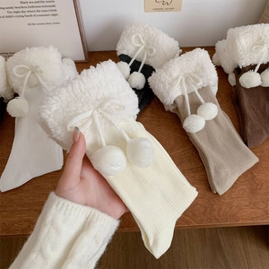 Close-up of knit winter socks featuring plush lamb wool cuffs and decorative pom-pom bows