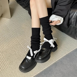 Detail of black platform loafers with white satin bows and ribbed leg warmers
