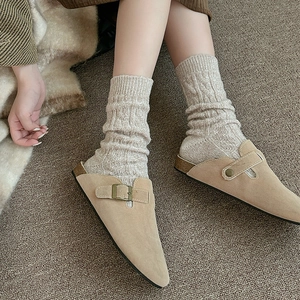 Détail de mules en daim beige avec boucles portées avec des chaussettes en laine torsadée