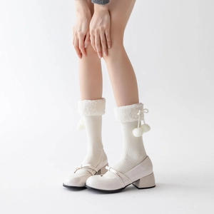Detail of cream knit mid-calf socks with white faux fur trim and fluffy pom-pom charms