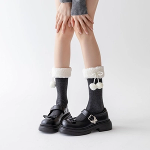 Macro detail of dark grey knit socks featuring white fluffy faux fur trim and pom-poms