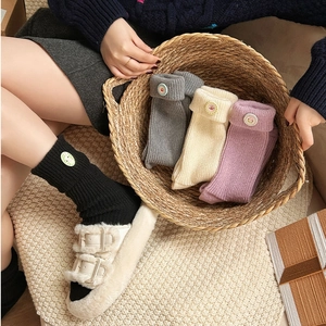 Close-up of knit crew socks with decorative floral buttons and folded cuffs in various colors