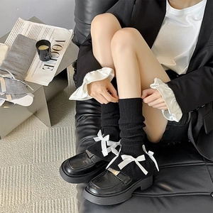 Detail of black knit leg warmers featuring white ribbons and bows in balletcore style