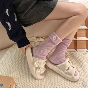 Detail of light purple ribbed socks with cute white flower buttons and plush beige slippers