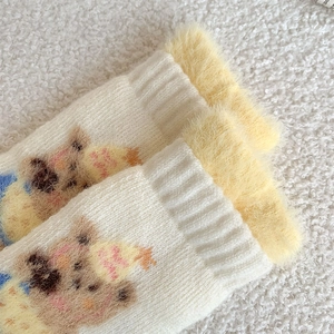 Close-up of white plush socks featuring a cute brown bear pattern and yellow faux fur cuff