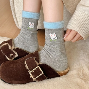 Détail de chaussettes grises avec broderie lapin et revers pelucheux bleu clair et pantoufles