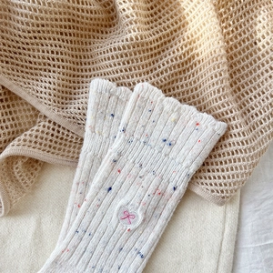 Detail of cream wool socks with colorful speckles and embroidered pink bow accent