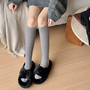 Detailed knit texture of grey ribbed calf socks paired with black plush slippers
