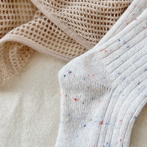Close-up of white ribbed wool socks with colorful confetti yarn and bow embroidery