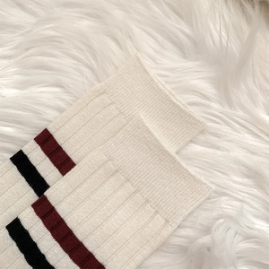 Detail of white ribbed mid-calf socks with burgundy and black stripes on a plush surface