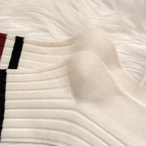 Close-up of cream ribbed cotton socks with red and black stripes on fuzzy background