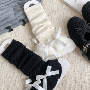 Detailed knit texture of rib-stitch leg warmers with silk bow accents in neutral tones