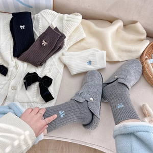 Détail de chaussettes en maille côtelée avec broderie nœud en noir, marron, crème et gris