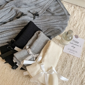 Close-up of knit leg warmers with ribbon bows in black, grey, and beige colors