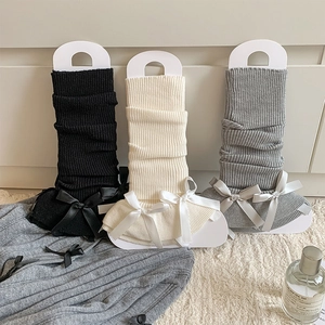 Detail of ribbed knit leg warmers with satin bows in black, beige, and grey colors