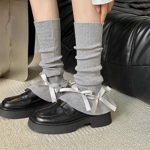 Detail of grey knitted leg warmers with satin bows and ruffle trim on black loafers