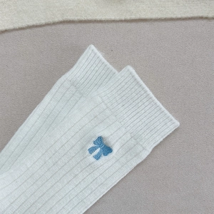 Détail de chaussettes blanches en maille côtelée avec broderie nœud bleu clair délicate
