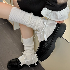 Detail of white rib-knit leg warmers with satin bows paired with black platform shoes