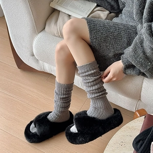 Detail of grey knitted thermal socks and black plush slippers in a cozy home setting