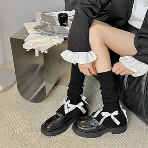 Detail of black knit leg warmers featuring white satin bows and leather loafers