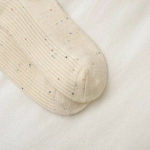 Makroaufnahme von cremefarbenen Stricksocken mit bunten Sprenkeln und Rippenstruktur