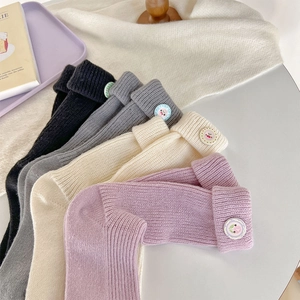 Detail of ribbed knit socks with folded cuffs and cute cartoon buttons in soft colors