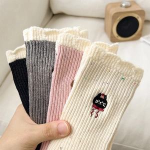 Detail von Stricksocken mit Rüschenrand und süßer Katzenstickerei in sanften Pastelltönen