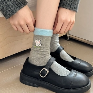 Détail de broderie lapin blanc sur chaussettes grises avec bordure en peluche