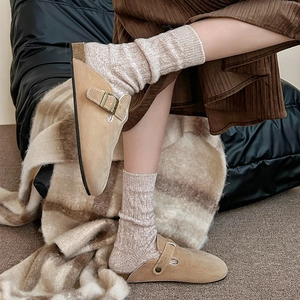 Détail d'une mule en daim kaki portée avec des chaussettes en laine et une jupe