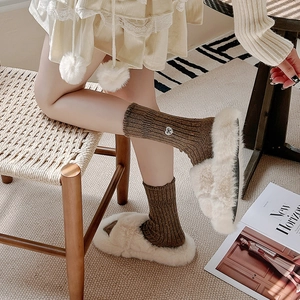 Detailed close-up of thick brown wool socks with heart embroidery and beige plush slippers