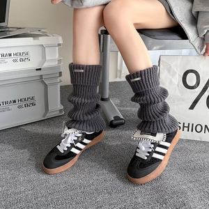 Close-up of dark grey cable knit leg warmers with metallic logo detail for women