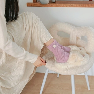 Close-up of purple ribbed knit socks with yellow smiley face embroidery and plush slippers