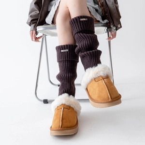 Detail of dark brown knitted leg warmers with silver metal tag and plush slippers