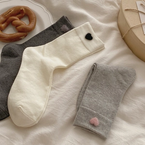 Detail of grey knitted mid-tube socks with cute 3D plush heart patch in cozy setting