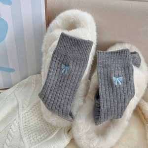 Détail de chaussettes côtelées gris foncé avec broderie nœud bleu sur pantoufles en peluche