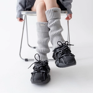Detailed view of grey thick knit leg warmers with silver metal logo and vertical stripes