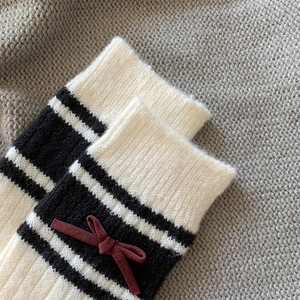 Detail of knit wool leg warmers featuring red bow accents and black striped pattern