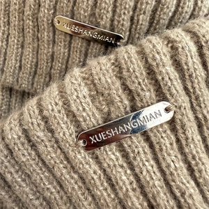 Detail of oatmeal chunky knit leg warmers featuring a silver metallic brand logo tag