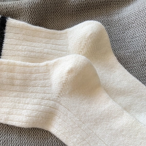 Detailed close-up of white wool blend knit socks featuring black stripe and ribbed texture
