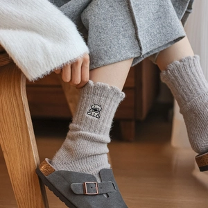 Detail of gray knitted socks with puppy embroidery and lettuce trim in a cozy setting