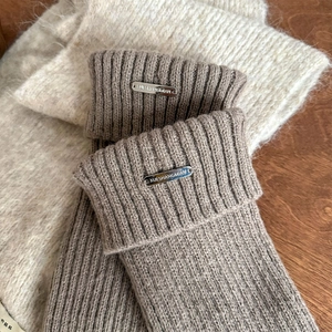 Close-up of thick rib knit leg warmers in grey with a stylish silver metal logo plate
