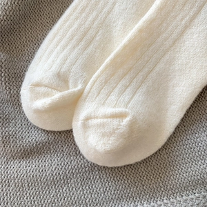 Detailed close-up of cream knit wool socks with vertical ribbed texture and fine toe seams