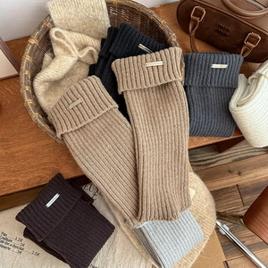 Detail of thick ribbed knit leg warmers with metallic brand tags in assorted colors