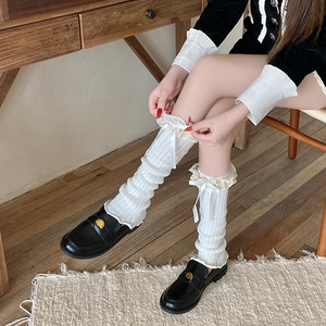 Close-up of white knitted leg warmers with lace trim and ribbon bows for women