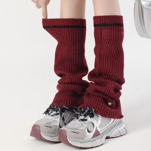 Close-up of deep red knitted leg warmers with black stripe and ribbed texture detail